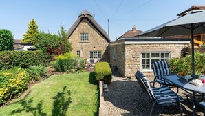 A stone house with a thatched roof, a gravel patio, and outdoor seating. - 18th century thatched Cotswold holiday cottage in Broadway - Orchard Cottage, Broadway (Broadway)
