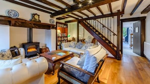A cozy living room with a fireplace, a sofa set, a wooden staircase, and a bookshelf. - Family friendly period holiday cottage in the Cotswolds - Summer Hayes (Childswickham near Broadway)