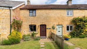 A stone house with a wooden door, a small garden with flowers and a wooden fence. - Family friendly period holiday cottage in the Cotswolds - Summer Hayes (Childswickham near Broadway)