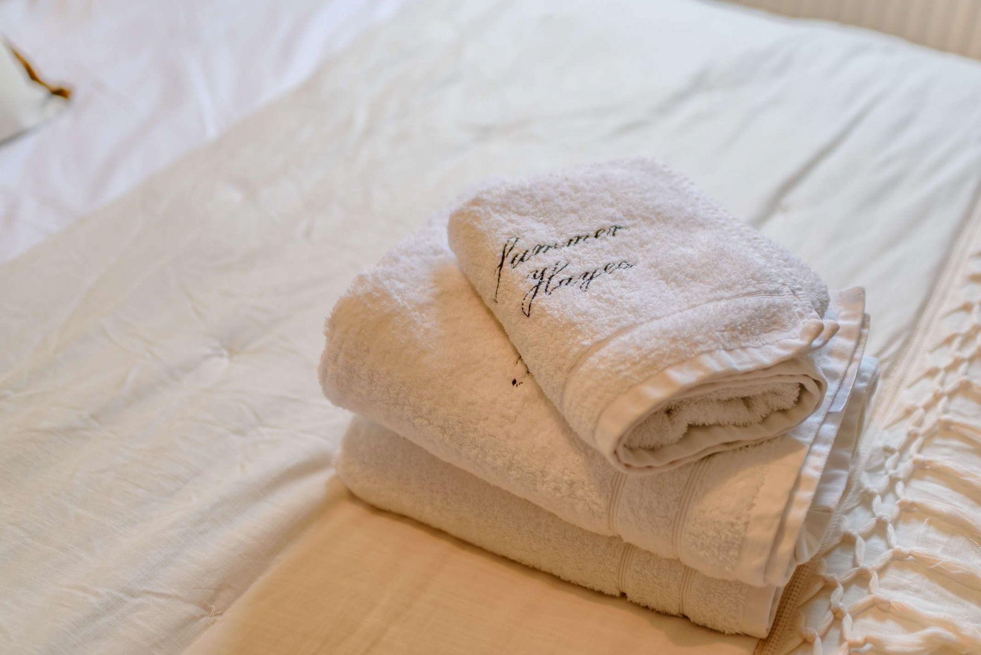 A neatly folded white towel with "Summer Flowers" embroidered on it, placed on a bed with a white bedspread.