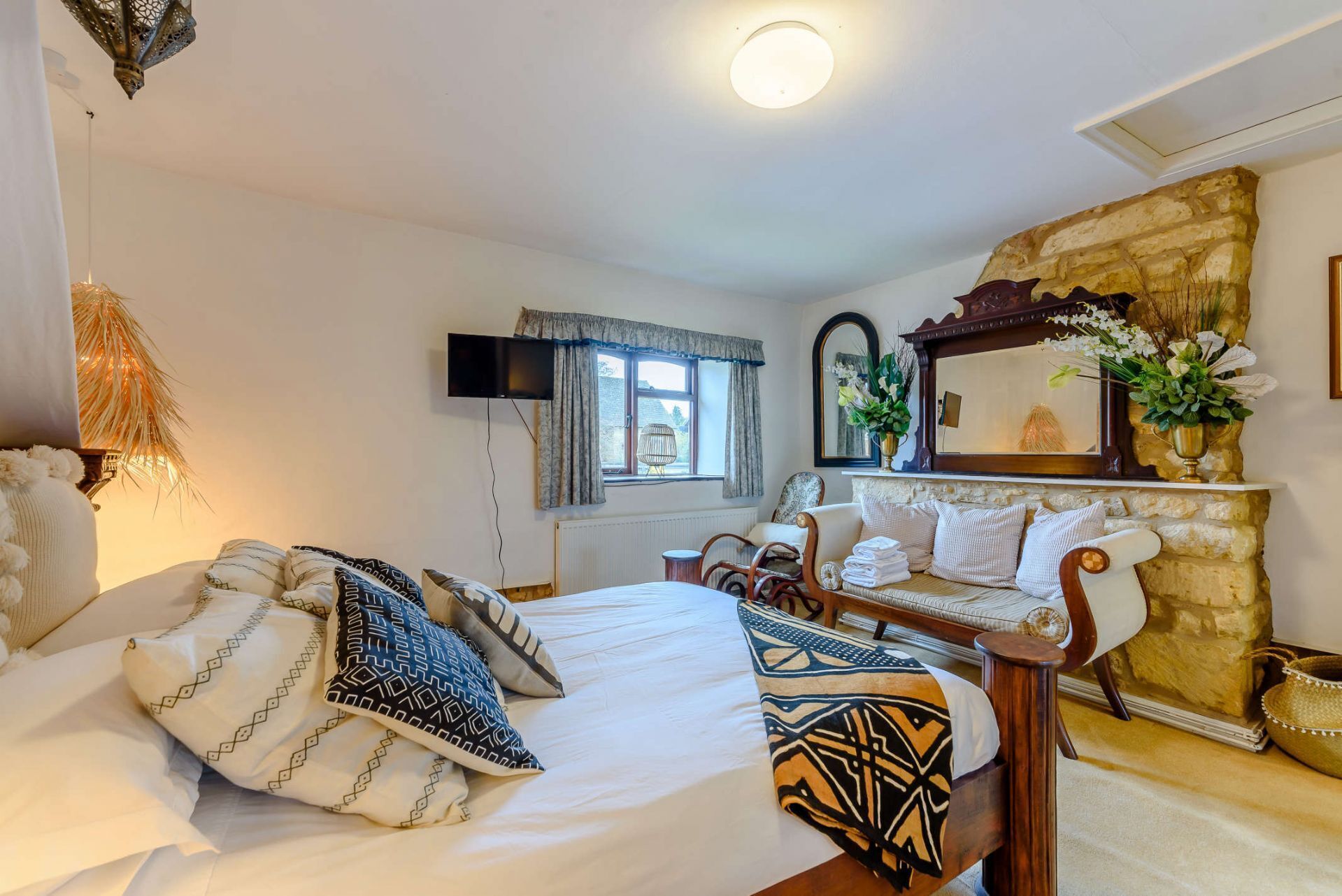 Ein gemütliches Schlafzimmer mit Bett, Nachttischen, Fernseher und einer Steinwand.