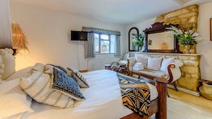 A cozy bedroom with a bed, bedside tables, a TV, and a stone wall. - Family friendly period holiday cottage in the Cotswolds - Summer Hayes (Childswickham near Broadway)