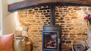 A stone wall interior with a wood-burning stove, wicker baskets, and a fireplace. - A delightful two bedroom Cotwold holiday cottage with garden - Cosy Corner (Moreton-in-Marsh)
