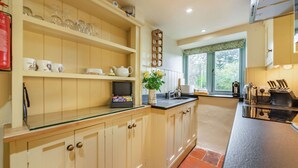 A kitchen with wooden cabinets, a glass countertop, a window with a view, and a stove. - A delightful two bedroom Cotwold holiday cottage with garden - Cosy Corner (Moreton-in-Marsh)