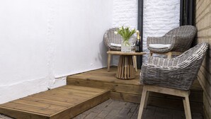 A small outdoor seating area with wicker chairs and a table, a bottle of champagne, and a vase with flowers. - Elegant family friendly holiday cottage in the Cotswolds - The Smithy (Chipping Norton)