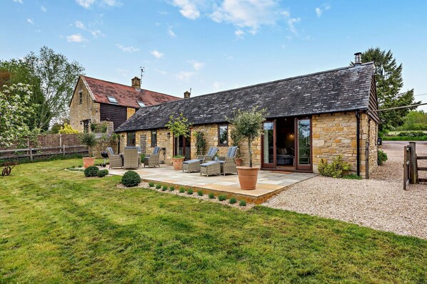 A stone building with a tiled patio, outdoor seating, and a grassy yard.