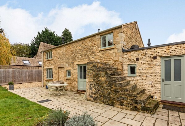 A stone house with a patio, a dining table, and a small garden.