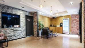 Eine Lobby mit einer Rezeption, einer Sitzecke mit Pflanze, einem Kühlschrank und einem Schild für eine Snackbar.