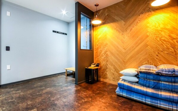 A hotel room with a herringbone wood wall, a wooden floor, a bed with plaid bedding, a bedside table with a lamp, and a phone on the table. - Yeosu Hotel The B (Yeosu)