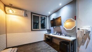 Ein kleines Hotelzimmer mit Schreibtisch, Spiegel, Fön, Fenster und integrierter Klimaanlage.