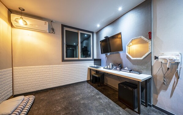 A compact hotel room with a small desk, a mirror, a hairdryer, a window, and a built-in air conditioner. - Yeosu Hotel The B (Yeosu)