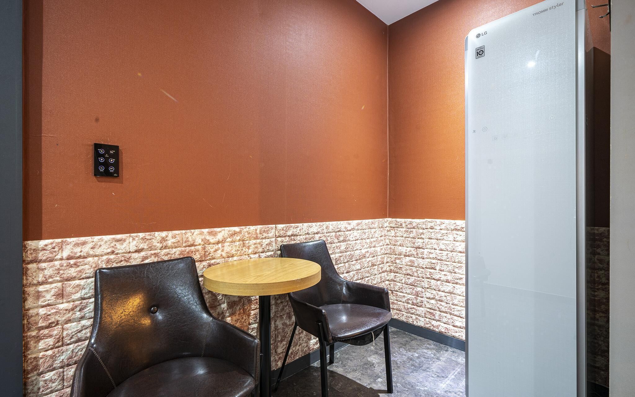 A corner room with a brick accent wall, a small round table, two leather chairs, and a white door.