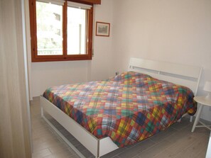 Un dormitorio con cama, ventana, mesita de noche y un cuadro en la pared.