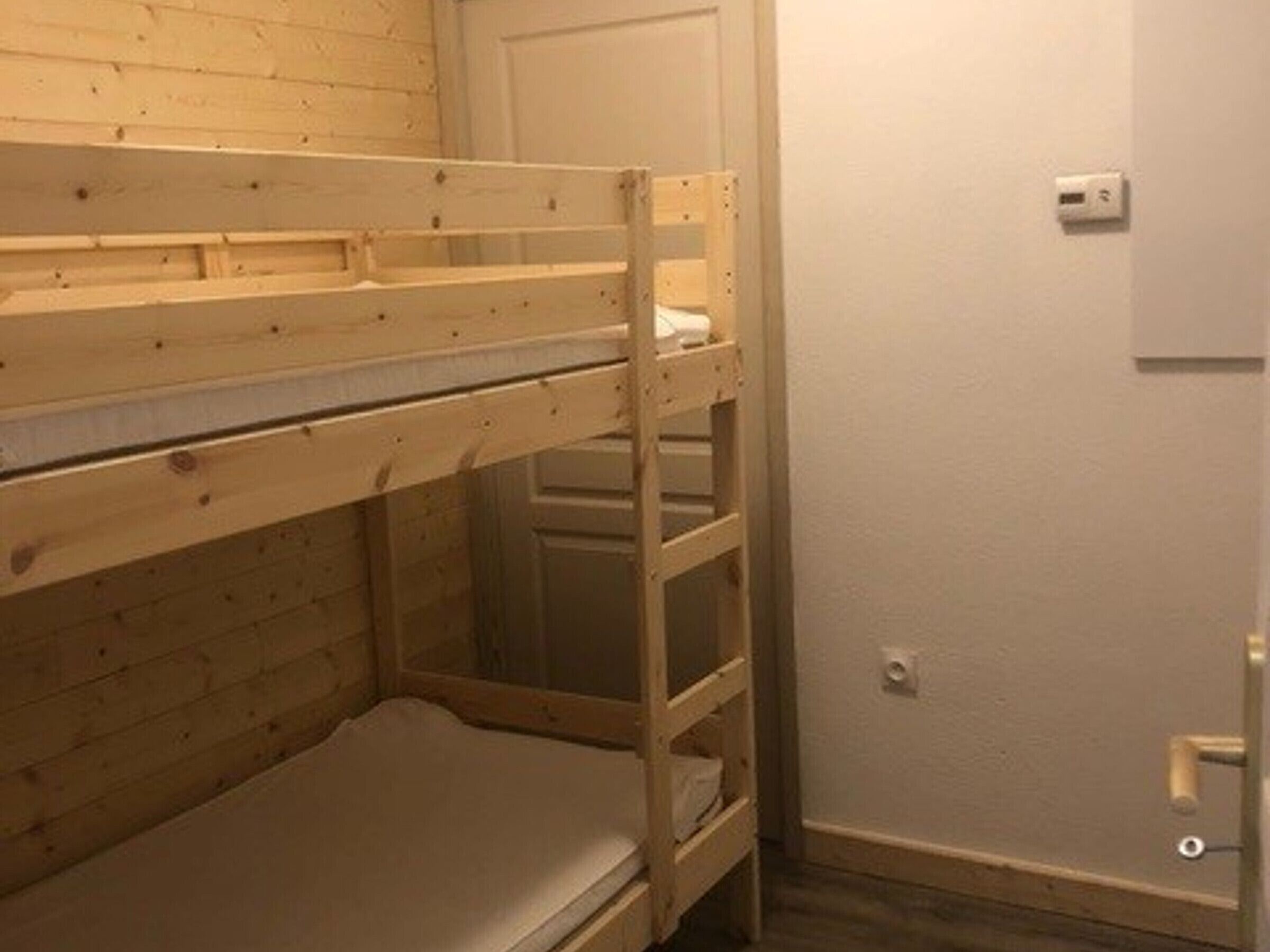 Et værelse med køjeseng i træ, en hvid dør og en lyskontakt på væggen.