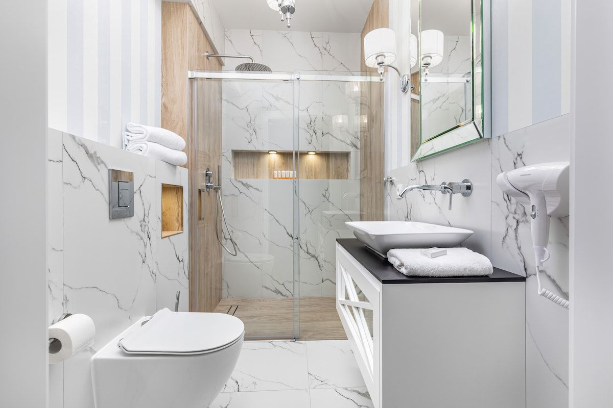 Un baño moderno con ducha envuelta en vidrio, inodoro blanco, tocador con un espejo grande y un secador de pelo.