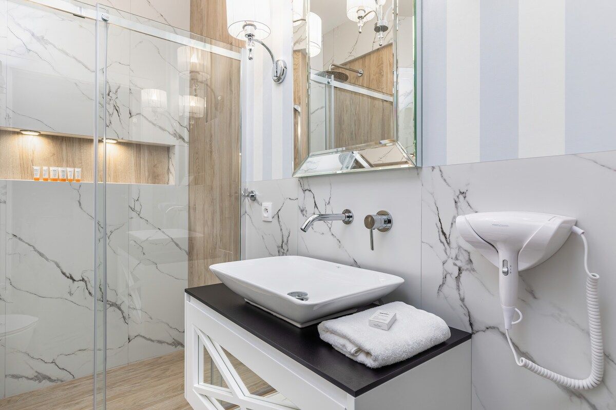 Ein modernes Badezimmer mit einem мраморным Waschbecken, einem Handtuch, einem Föhn und einer Duschkabine aus Glas.
