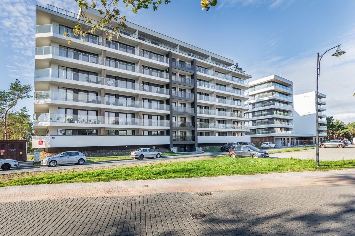 Un immeuble résidentiel à plusieurs étages, doté de balcons, d’une allée pavée et de voitures garées.