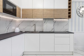 A modern kitchen with white cabinetry, a black countertop, a built-in microwave, and a marble backsplash.