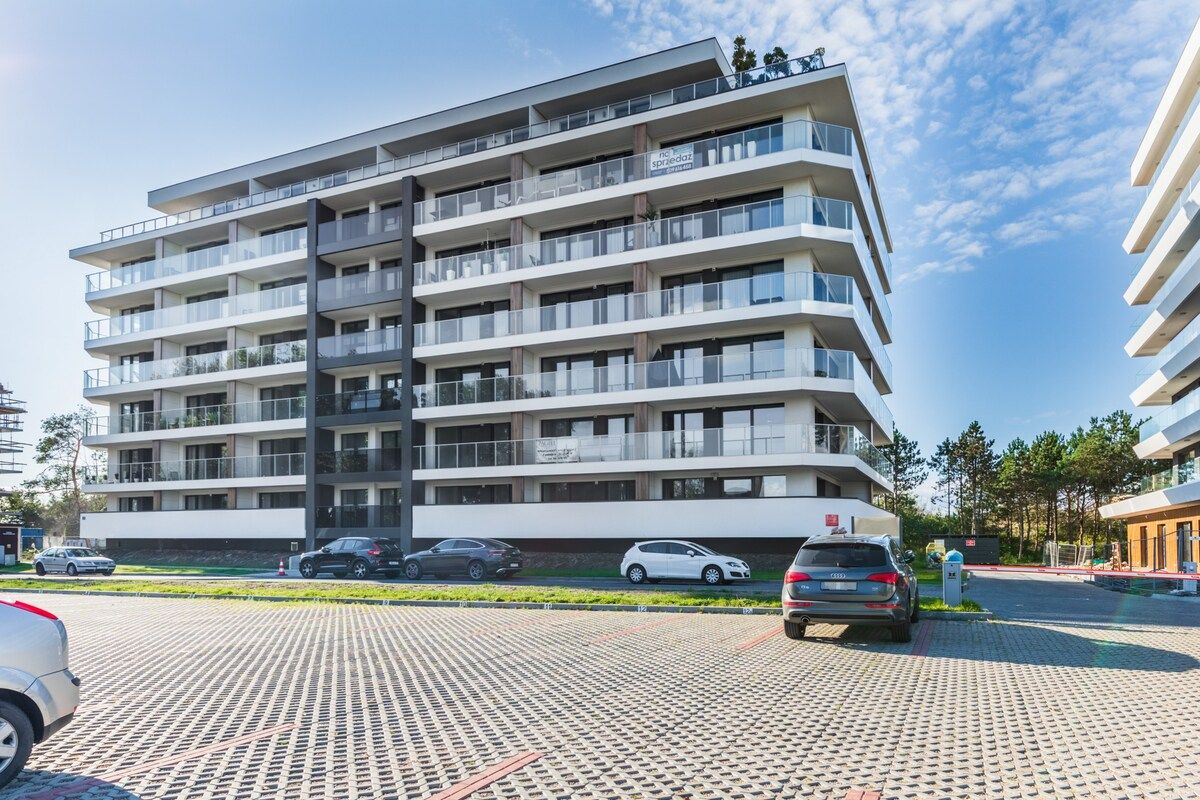 Ein mehrstöckiges Gebäude mit Balkonen, einem Parkplatz und blauem Himmel.