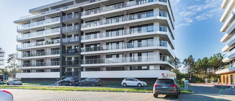 Un edificio de varios pisos con balcones, una zona de estacionamiento y cielo despejado.