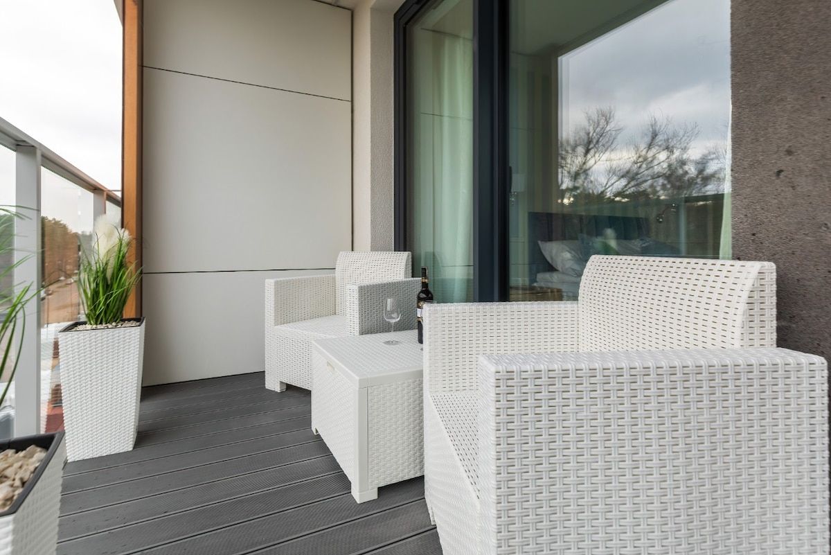 Un balcon agrémenté de meubles en osier blanc, notamment d’un canapé et d’une table, ainsi que d’une plante en pot.