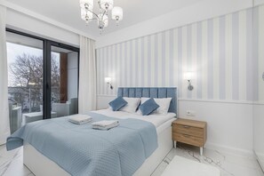 Une chambre moderne avec un grand lit, une table de chevet, un lustre et une vue sur l’extérieur, accessible par une porte coulissante.