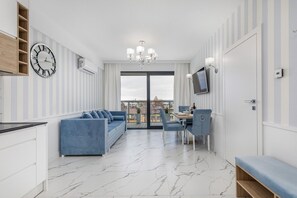Un salon moderne comprenant un canapé, une table à manger, des chaises, un téléviseur et une grande fenêtre.