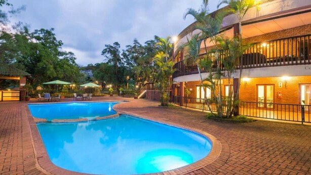 A swimming pool area with a brick pathway, lounge chairs, and a building with a balcony. - Greenway Woods Self Catering Unit no 9, Whiteriver (Mbombela)