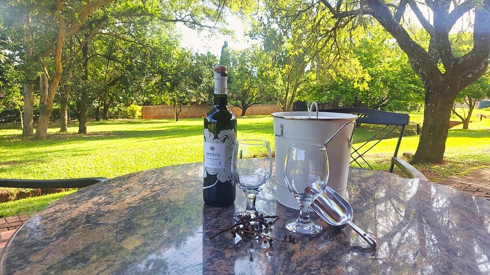 Una botella de vino, una copa de vino y un balde de metal sobre una mesa al aire libre.