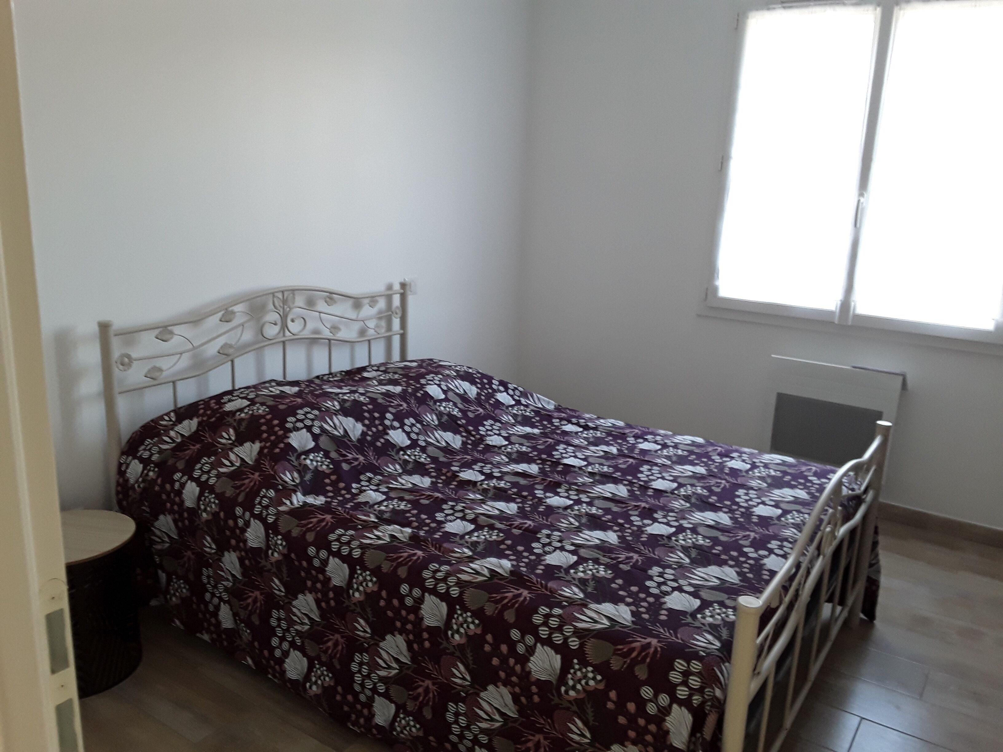 A single bed with a floral bedspread in a room with a window, a radiator, and a small round table.
