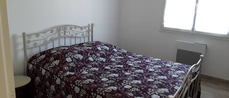 A single bed with a floral bedspread in a room with a window, a radiator, and a small round table.