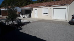 Un garaje residencial con camino de entrada de grava, un porche cubierto con mobiliario exterior y una puerta de garaje blanca.