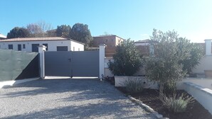 Un camino de grava que conduce a una entrada porticada con un muro blanco y un pequeño árbol.