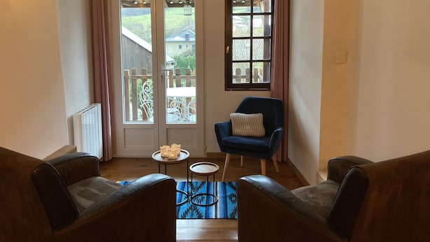 Una habitación acogedora con un amplio ventanal corredero que da a un balcón, una pequeña mesa redonda con una vela y dos sillones.