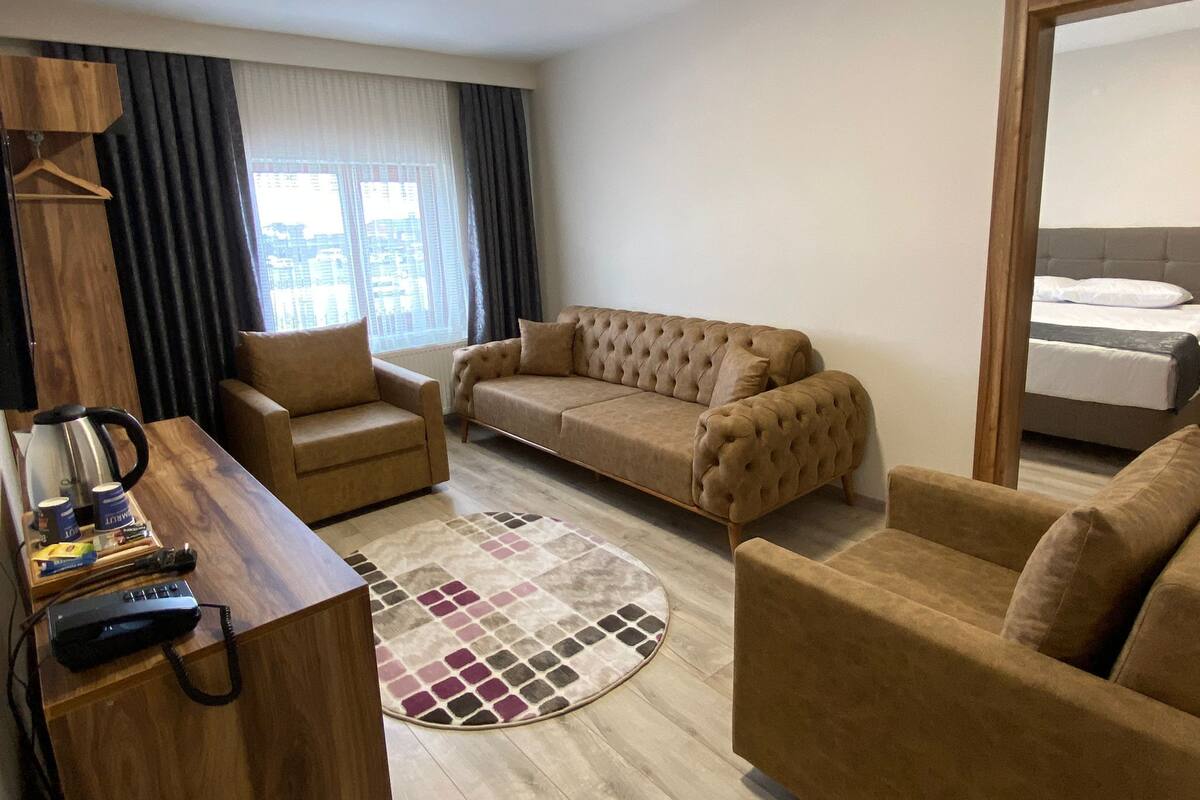 Uma sala de estar moderna com sofá, poltrona e uma mesa lateral de madeira com chaleira e controle remoto.