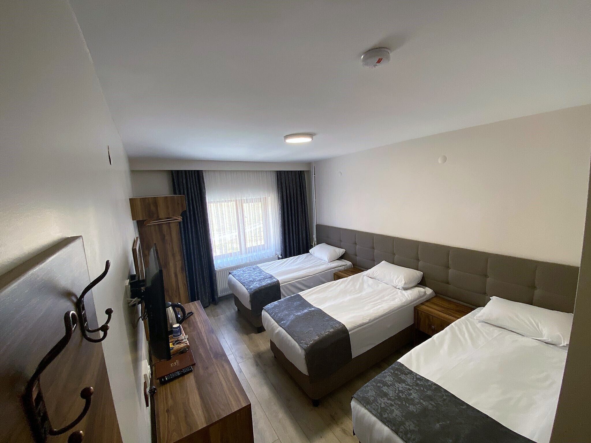 Una camera d'albergo con due letti singoli, una scrivania con sedia, un armadio e una finestra con tende.