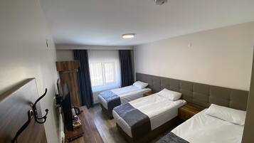 Una camera d'albergo con due letti singoli, una scrivania con sedia, un armadio e una finestra con tende.