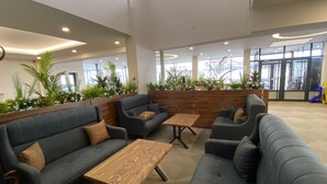 A modern lobby with grey sofas, wooden tables, and green plants. - Zumrut Palas Hotel (Kayseri)