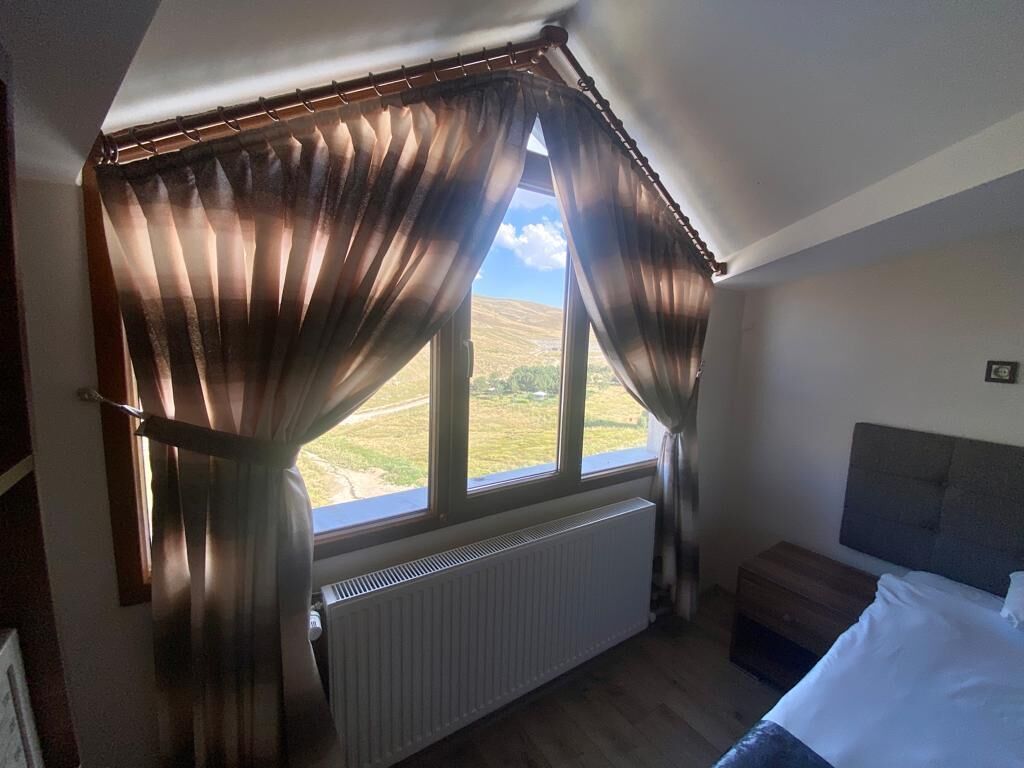 A bedroom with a large window, a radiator, a bed, and a bedside table.
