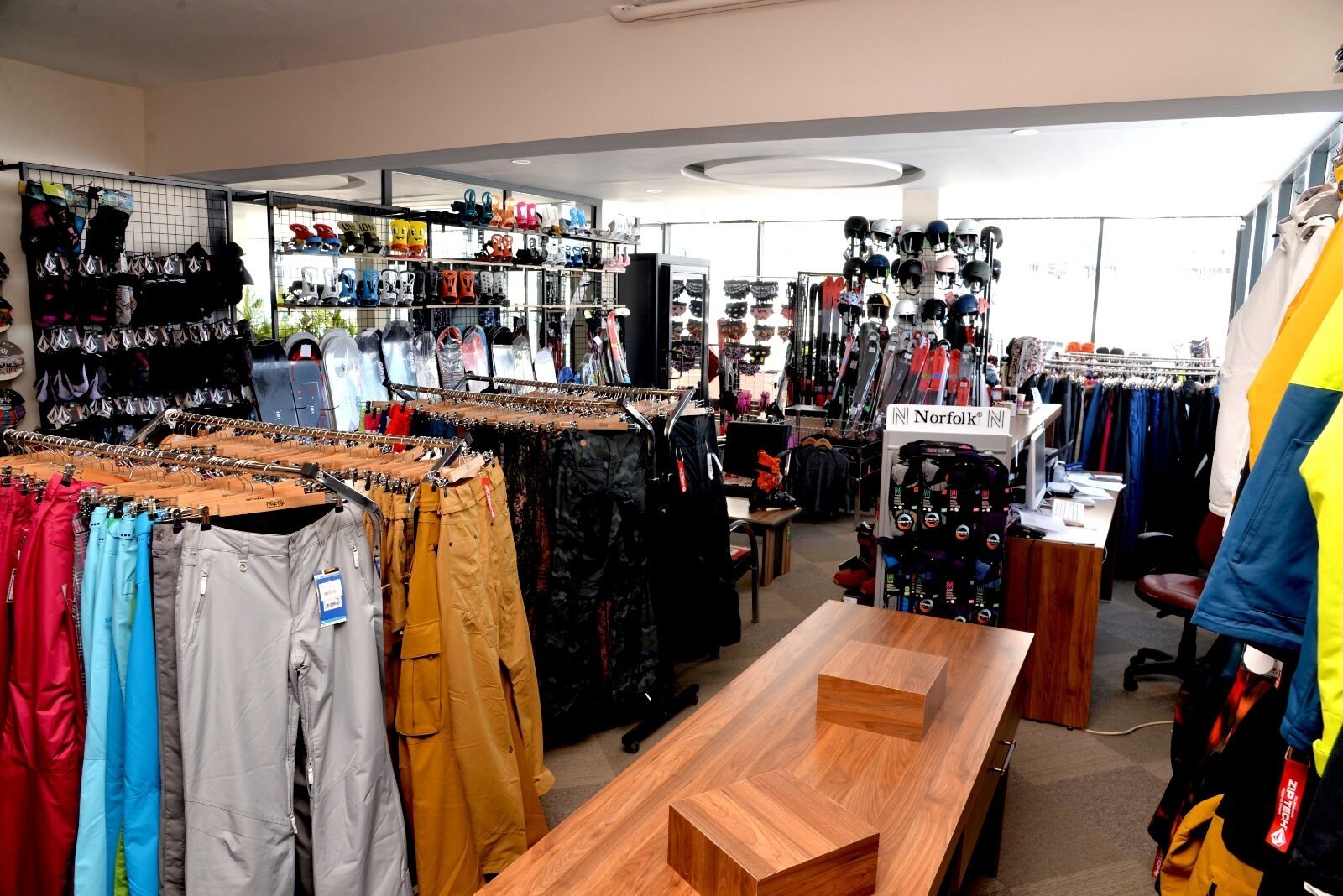A retail store with various clothing items on racks and shelves, including jackets and pants.