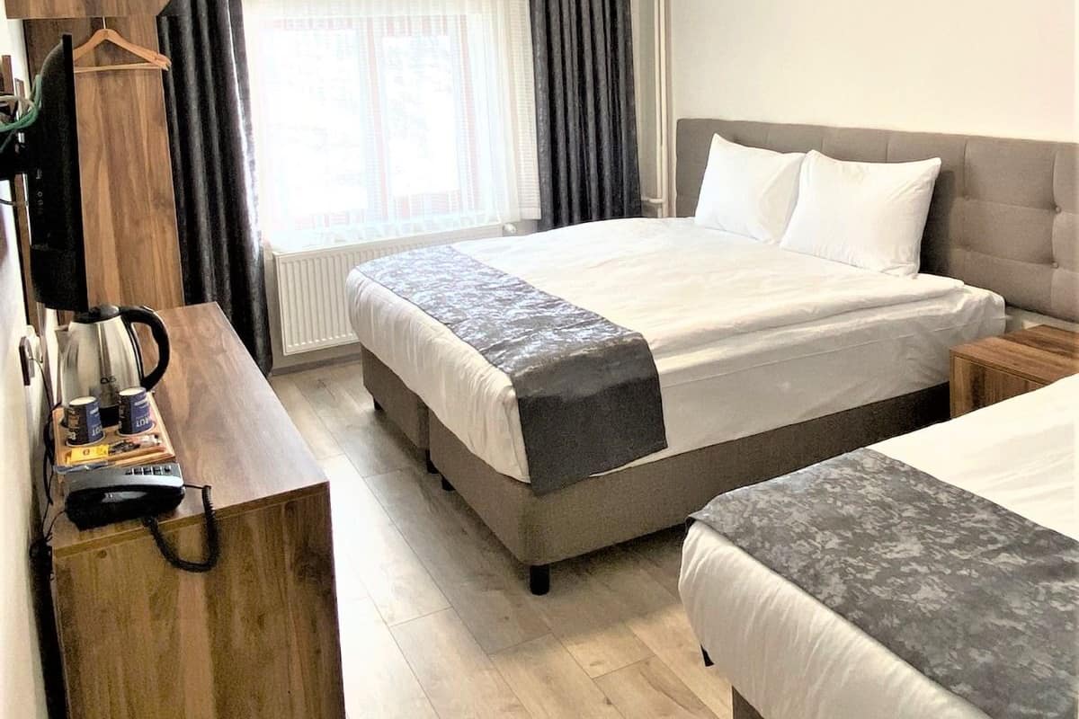 Quarto de hotel com uma cama grande, uma escrivaninha com cafeteira e vista para a cidade pela janela.