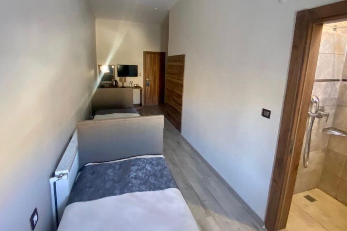 A narrow hallway leading to a bedroom with a bed, a small table, and a mirror.