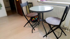 A small dining area with a round table and two chairs, a radiator, and a window with curtains. - Vacation Apartment Near The Black Forest (Villingen-Schwenningen)