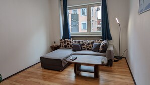 A small, cozy room with a sofa, a small table, and a window with curtains. - Vacation Apartment Near The Black Forest (Villingen-Schwenningen)
