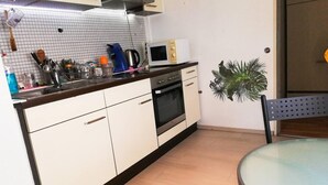 A compact kitchen with white cabinets, a microwave, a kettle, and a dining table with a chair. - Vacation Apartment Near The Black Forest (Villingen-Schwenningen)