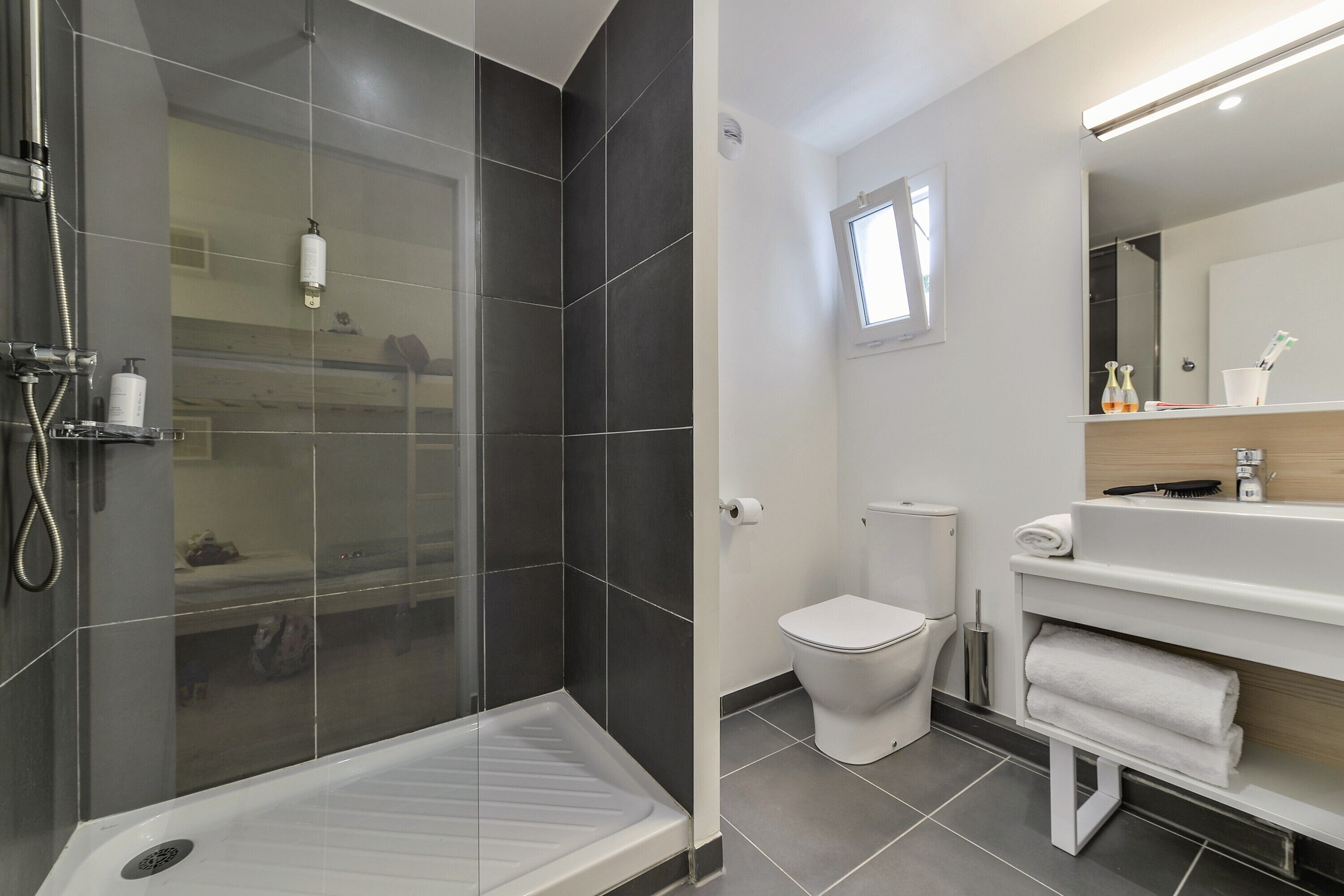Un baño moderno con ducha envuelta en vidrio, inodoro blanco y tocador con espejo y toallero.