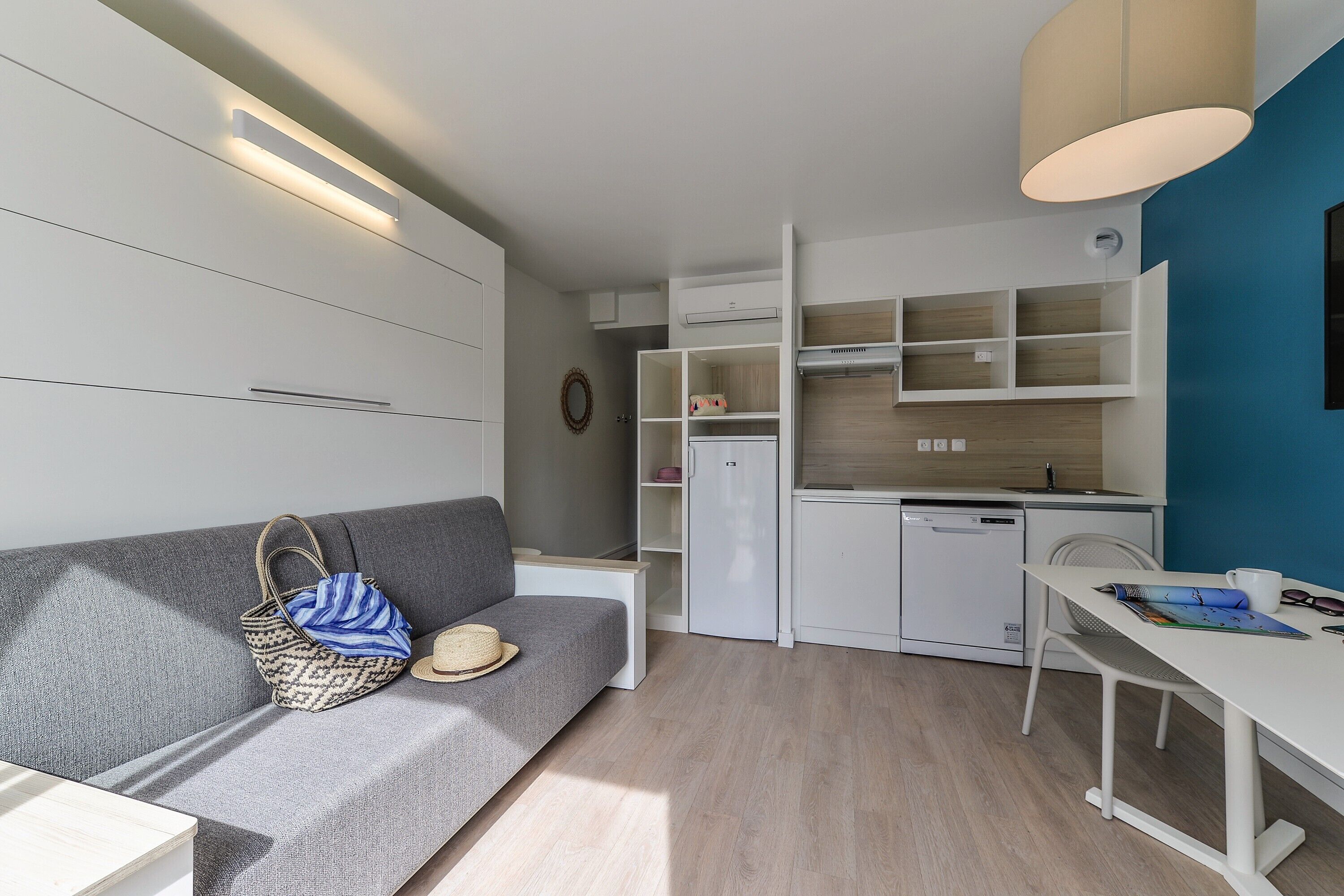 Un espace de vie compact comprenant un canapé, une table à manger, un coin cuisine et des étagères intégrées.