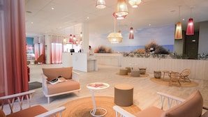A modern hotel lobby with a reception desk, seating area, and a view of the ocean. - Belambra Clubs Port Camargue - Les Salins (Le Grau-Du-Roi)