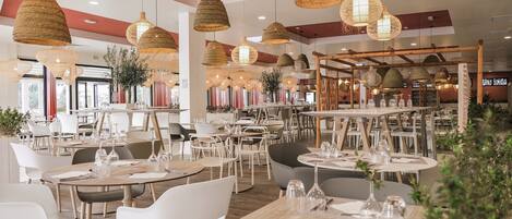 Un restaurante moderno con mesas redondas, sillas blancas y lámparas colgantes tejidas.