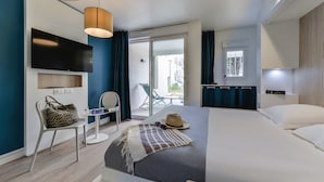 A modern hotel room with a bed, a TV mounted on the wall, a chair, a small table, and a view of the outside balcony. - Belambra Clubs Port Camargue - Les Salins (Le Grau-Du-Roi)
